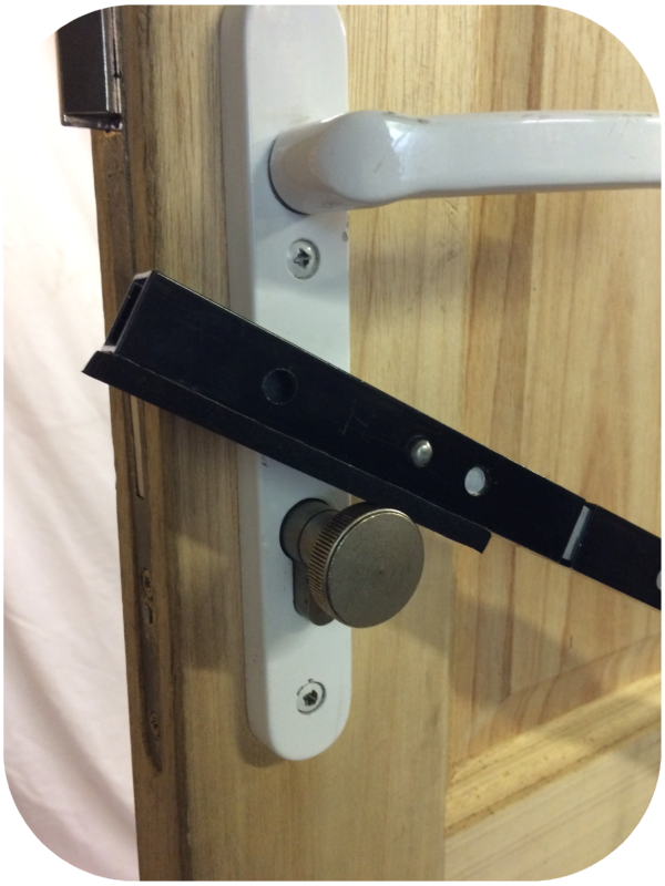 Close-up of white door handle with lock inside and black metal bar resting on the lock knob
