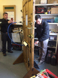 Locksmith trying out tools on test door at a training session while Mark takes a photo