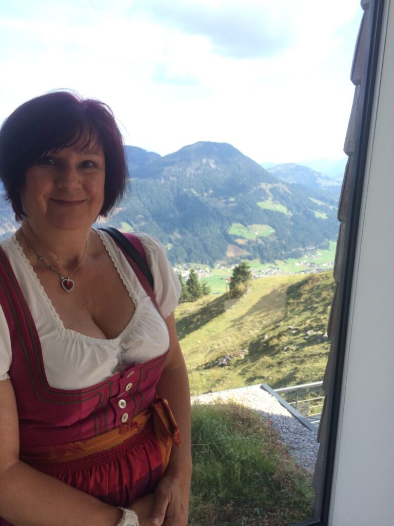 Attractive lady dressed in dirndl leaning against side with mountains in the background